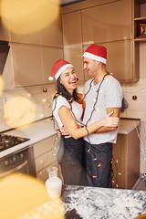 Couple with santa hats standing on the kitchen together indoors