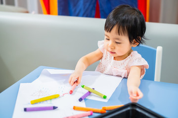 Asian baby girl is drawing with colorful crayons at home
