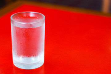 glass of cold water with water drop around the glass  on red table background