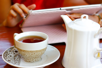 tea cup and white teapot and blur hand holding tablet and one finger touch on screen of tablet