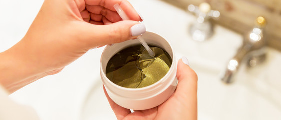 Female hands are taking eye patches out from the container with the tweezers. Anti aging concept