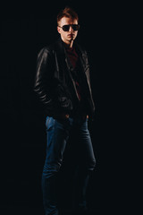 Portrait of a young guy in sunglasses and a leather jacket on a black background.