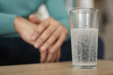 Close-up of glass with painkiller on the table with man sitting in the background