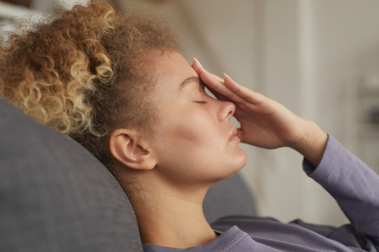 Young woman with curly hair lying on sofa with headache she is very tired