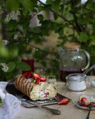 Biscuit roll, decorated with strawberries, on the Board, on the table in the garden under the cherry tree.