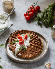 Unsweetened rice waffles with garlic sauce and cherry tomatoes on a plate.