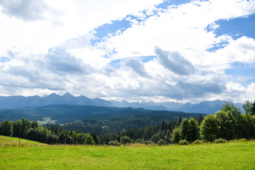 Fototapeta na wymiar Beautiful green grassland and distant blue mountains against dramatic sky background on a nice summer day somewhere in Tatra Mountains in Poland