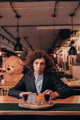 young curly-haired guy in a black suit drinking a liqueur in the bar