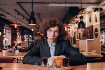 young curly-haired guy in a black suit drinking a liqueur in the bar