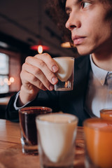 young curly-haired guy in a black suit drinking a liqueur in the bar