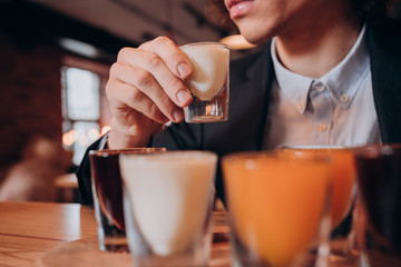 young curly-haired guy in a black suit drinking a liqueur in the bar