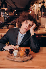 young curly-haired guy in a black suit drinking a liqueur in the bar
