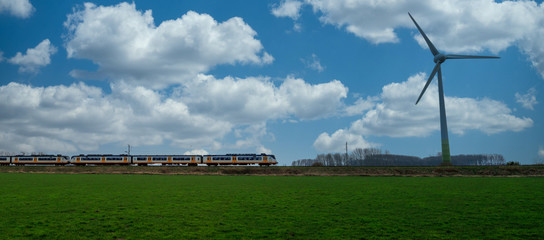 Wind turbine, blue sky with clouds and passenger train