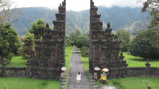 Back view of tourist woman walking through bali traditional gate in bedugul Traditional Balinese Hindu gate Candi Bentar, Bali island, Indonesia. Aerial view