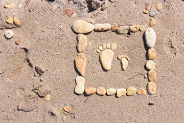 touching picture of sea pebbles on  sandy beach. Image of a child's and adult's foot made of stones. Ebbles and sand in the sea. Card. Background.