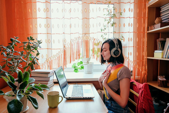 Female in headphones sits at front of laptop and breathing. Online audio meditation concept.