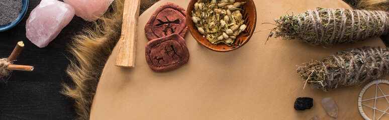 Top view of smudge sticks and crystals, dreamcatcher and clay amulets on tambourine on dark wooden surface, panoramic shot