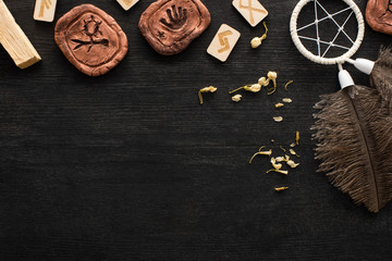 Top view of runes, dreamcatcher and dry flowers on dark wooden surface