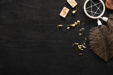 Top view of shamanic dreamcatcher, dry flowers and runes with signs on dark wooden surface