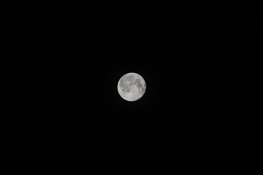 A very detailed photo of a bright full moon in the night sky on a full moon. A full supermoon in a black sky in the dead of night. The background of the full moon.