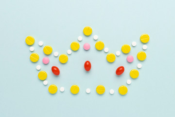 Crown made of colorful pills and tablets at blue background. Coronavirus creative minimal concept.