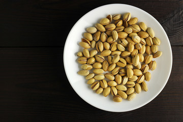 Macro pistachio nuts in shell in a white plate on a dark wooden background