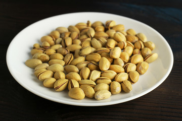Macro pistachio nuts in shell in a white plate on a dark wooden background