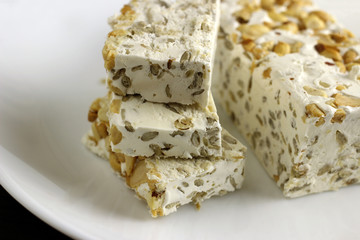 Pieces of sherbet or nougat with nuts in a plate on a dark wooden background