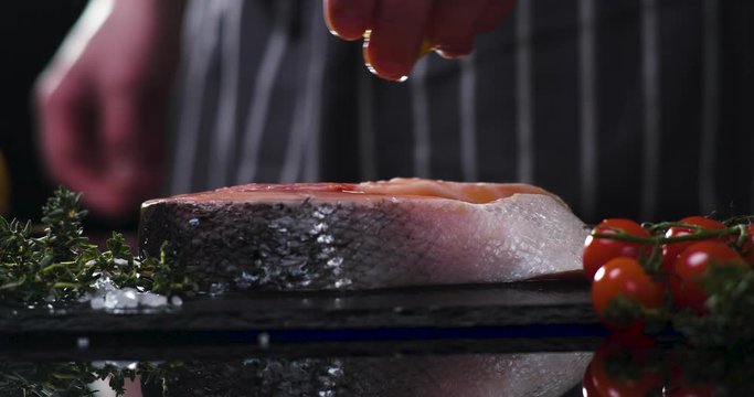 Closeup of preparing Salmon fillet, redfish a stone board. Tattooed Chef's hand squeezes a Lemon Juice on salmon&rsquo;s Fillet. Healthy Life conception. Healthy Eat. Professional Chef is cooking Seafood.