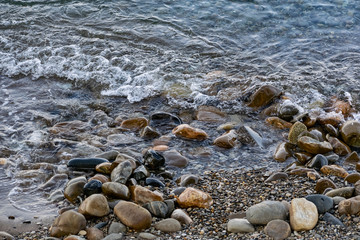 Large and smooth stones in the coastal waves of salty sea water. The coast of the black sea foams and roars, beating against a huge pebble, illuminated by sunlight