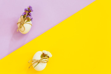 Trending white Easter eggs with flowers on a lilac and yellow background. Minimal concept