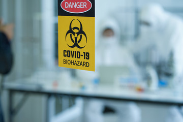 The COVID-19 warning sign on the glass of the clinical laboratory in hospital with the defocused blurred background of medical doctor scientists were doing research for VIRUS prevention and cure 