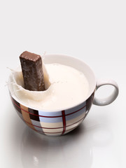 Chocolate bar falling and splashing into a cup of milk.
