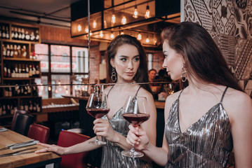 a beautiful young girl in a shiny dress with long hair stands at the mirror with a glass of red wine in her hand