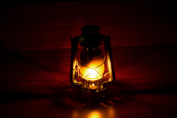 old kerosene lamp glows in a dark place against the shadows and wooden background.