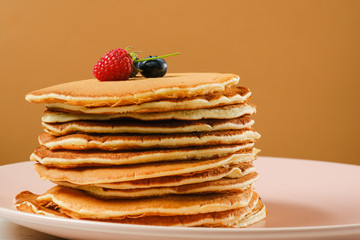 Stack of pancakes with berries.Copy space for your text. On a light brown background.