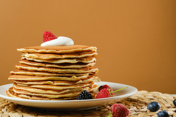 Stack of pancakes with cream and berries.Copy space for your text. On a light brown background.