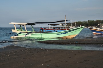 Small fishing boat on black beach on Bali island. 