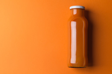 Carrot juice in a glass bottle on an orange gradient paper background. Minimalism. Image contains copy space