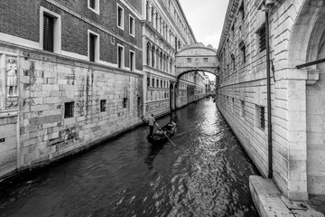 Fototapeta premium A typical Venetian gondola navigates the canal that passes under the famous Ponte dei Sospiri, Venice, Italy