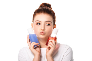 thoughtful teenager holding two bottles with red and blue makeup removers, isolated on white