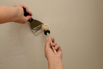 Woman plasterer repairing the wall with putty. With a brush, the master collects putty from the...