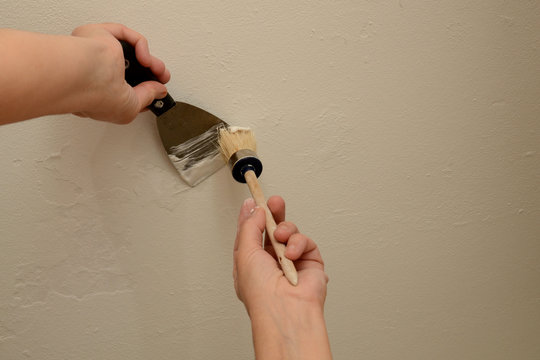 Woman plasterer repairing the wall with putty. With a brush, the master collects putty from the tool. Close-up, copy space.