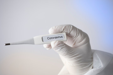 termometro con su scritto Coronavirus, tenuto da una mano con guanto su sfondo bianco