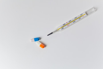 Obraz premium Thermometer and two capsules of orange and blue on a white table