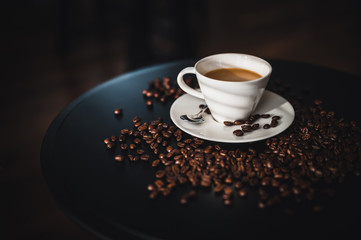 Coffee and coffee beans on black table.  Coffee beams closeup. Coffee theme. White cup on black table.