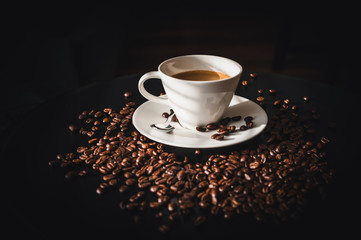 Coffee and coffee beans on black table.  Coffee beams closeup. Coffee theme. White cup on black table.