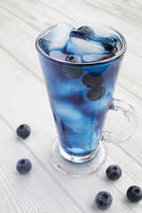 Glass of blue cocktail drink with ice and blueberry on the white wooden background. Location vertical. Closeup.