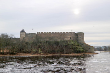 Fototapeta na wymiar Spring view to Ivangorod fortress on the river Narva with little cold sun in the sky