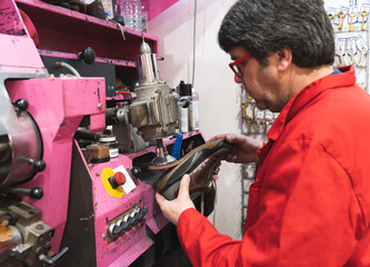 Shoemaker with red uniform and glasses filing the rubber sole of a shoe